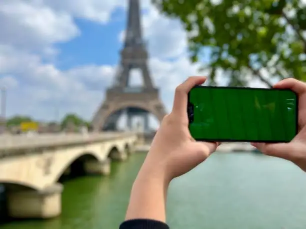 Photo of Phone with green Chromate screen on the background of the eiffel tower. in Paris using her cell phone in front of Eiffel Tower, seine bridge background,