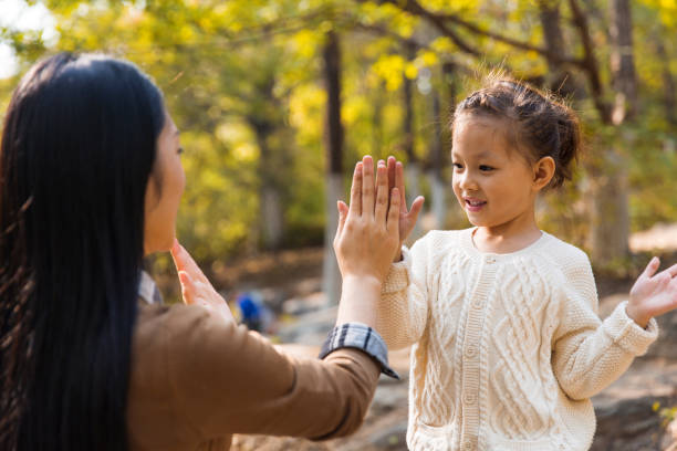 Cute little girl playing hand clapping game with her mother in the autumn forest and mountain stream - stock photo stock photo