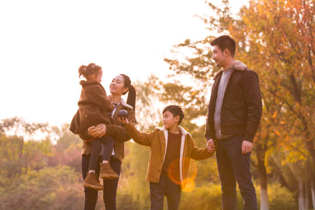 A happy young family of four by a colorful jungle at sunset in autumn, the mother holding her daughter - stock photo stock photo