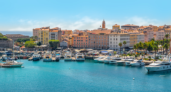 Bright image with boats and yachts in the harbor of Ajaccio, Corsica Island, France. Colorful buildings in the city along the waterfront. Blue sky on a summer day. Cruise destination. Panoramic landscape view.