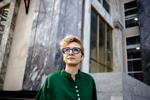 Lonely woman with asymmetric blonde hair wearing a green shirt with mandarin collar and glasses looking away in Hanoi, Vietnam