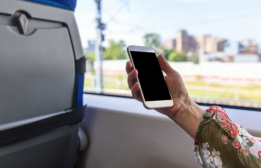 Woman hand holding smartphone with blank screen near the window inside train wagon