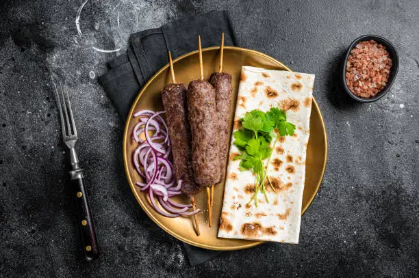 Lamb meat kofta kebab, onion and flat bread on plate. Black background. Top view.
