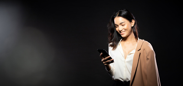 Half body portrait of Asian beautiful woman wear white shirt, using internet smart phone. Young female express feeling happy smile strong over black background isolated copy space