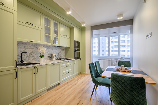 Modern trendy light green luxurious kitchen with dining table and dark green chairs