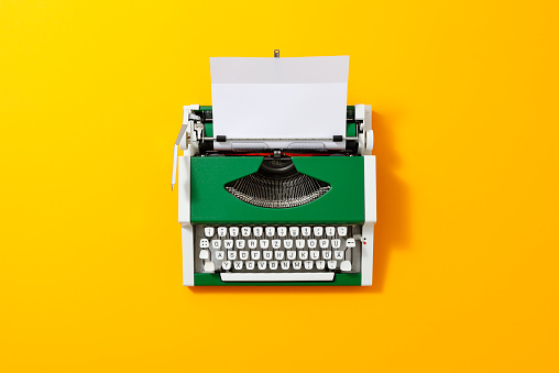 Green 70s typewriter with a blank page on yellow backround