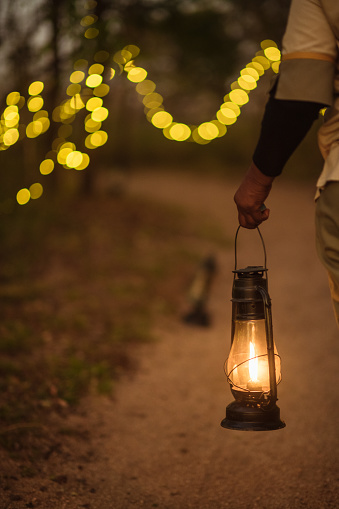 Walking down a path holding a lantern with string fairy lights