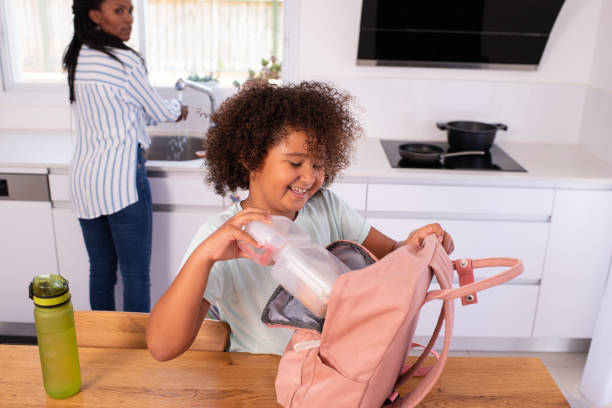 istock Happy elementary-age girl putting a lunch box into a pink backpack before going to school. 1412816523