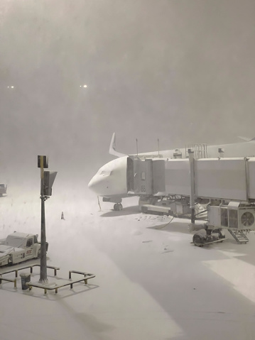 Airport, air traffic and safety concept: Looking from terminal building outside on cockpit connected to passenger boarding bridge on cold snowy winter day. Travel and Transportation theme background, copy space.