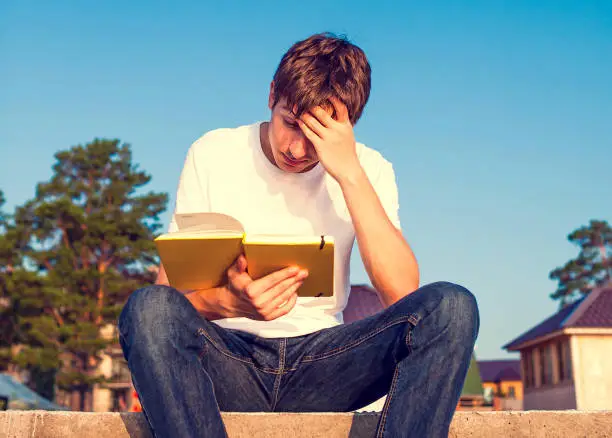 Toned Photo of Sad Young Man read a Book outdoor