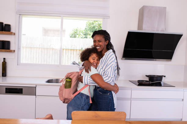 istock Happy mother and daughter with backpack hugging in the kitchen before going to school. 1412817889