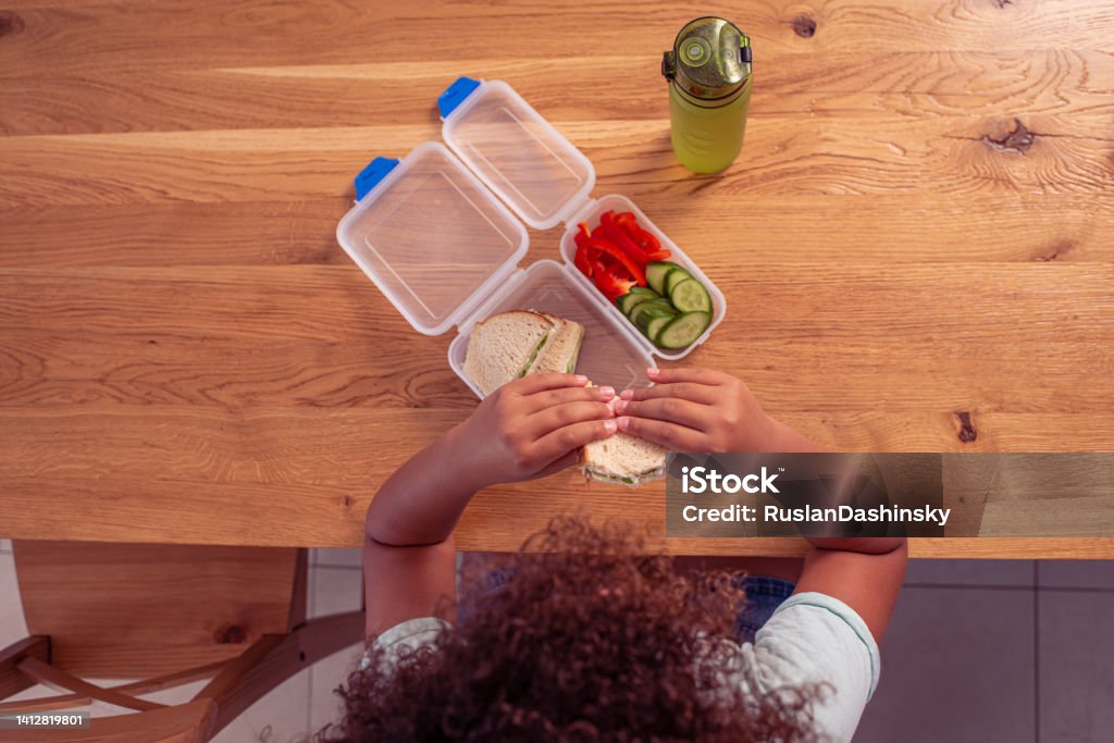 Top view image of a little student girl eating healthy lunch at school. Directly above image of a school girl eating healthy lunch during lunch break in classroom. Child Stock Photo