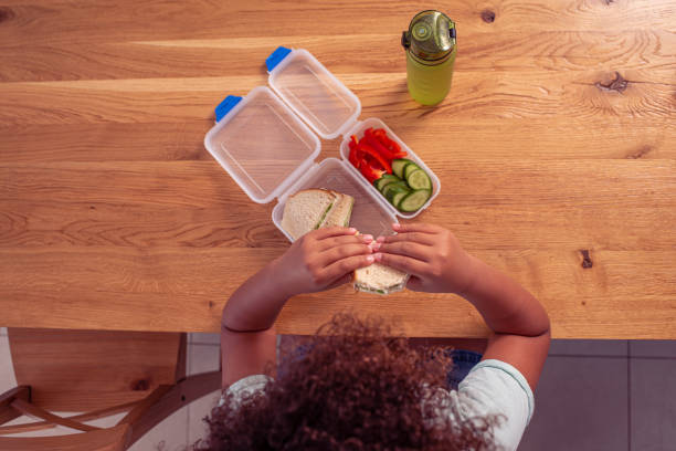 zdjęcie z góry przedstawiające małą uczennicę jedzącą zdrowy lunch w szkole. - refreshment dinner table vegetable zdjęcia i obrazy z banku zdjęć