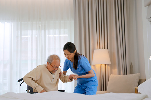 Nurse take care senior man in the bedroom. She bring him to the bed. Home healthcare concept.