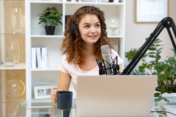 istock Young curly female recording podcast from home and talking into a microphone 1412819901