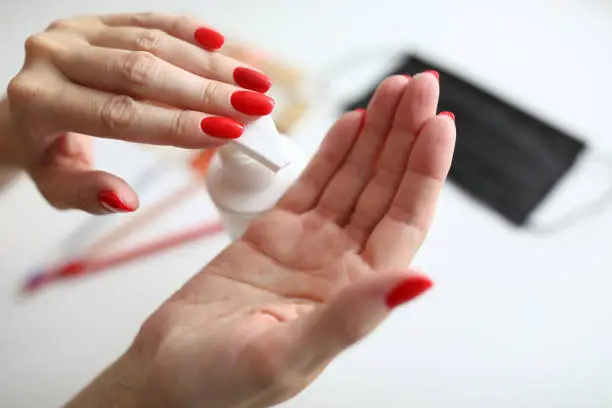Close-up of female pressing moisturizing lotion on hand. Woman smoothing hands. Beautiful bright red manicure. Taking care of skin. Beauty and cosmetics concept