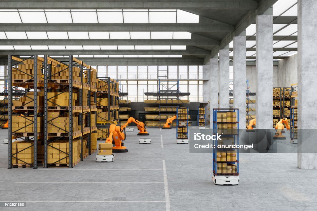 Distribution Warehouse With Automated Robots Putting Cardboard Box On AGV Robot Stock Photo