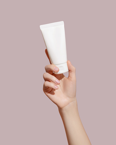 Hand holding blank white plastic tube on pink background. Cosmetic beauty product branding mockup. Copy space. High quality photo