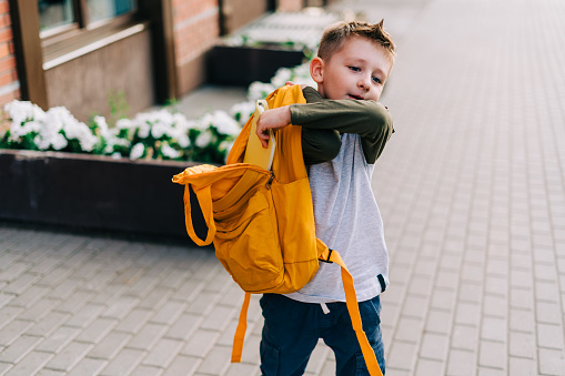 Back to school. Cute child packing backpack, holding notepad and training books going to school. Boy pupil with bag. Elementary school student going to classes. Kid walking outdoor on the city street.