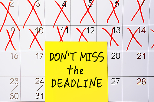 The phrase Dont miss the deadline written in black text on a yellow sticky note posted to a calendar page as a reminder. Close up of a personal agenda, top view. Motivational quote