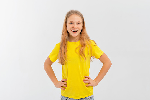 Smiling positive, attractive teen girl wearing casual yellow tshirt, feeling happy looking to camera standing isolated on white background