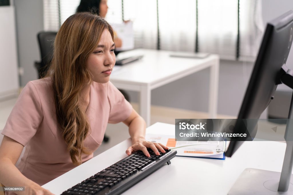 Asian female employee having farsighted problem looking at monitor, Blue light hazard from computer screen. woman tired of focusing on reading and working in the office. Myopia Stock Photo