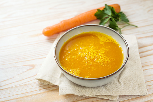Carrot soup in a bowl on a light wooden table, healthy vegetable meal, recipe by professor Ernst Moro against diarrhea, copy space, selected focus, narrow depth of field