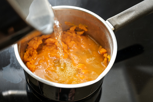 Pureed carrots are poured with boiling water in a steel pot, cooking a healthy digestible vegetable soup, invented by Professor Moro against diarrhea, motion blur, selected focus, narrow depth of field