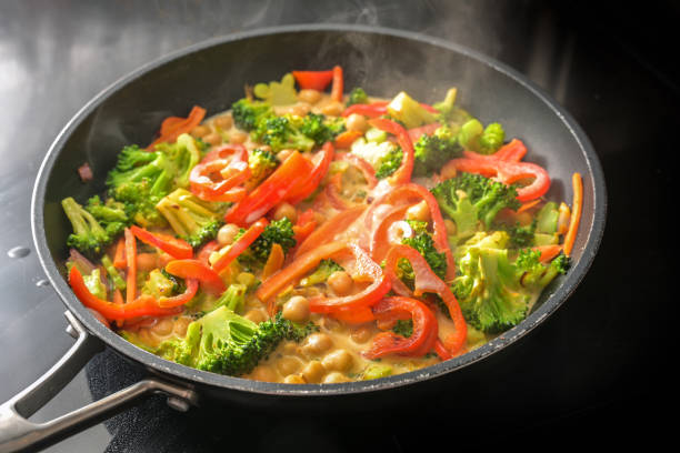 istock Steaming vegetable curry with chickpeas, broccoli and red bell pepper in coconut milk in a cooking pan on a black stove, healthy meals for a vegan low carb diet, copy space, selected focus 1412830059