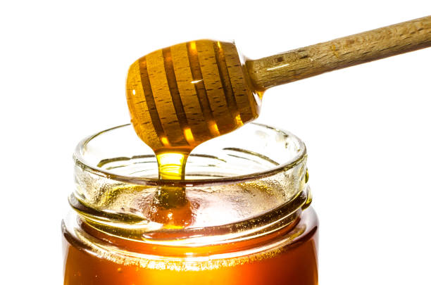 Getting honey from a jar with a honey spoon isolated on white background stock photo