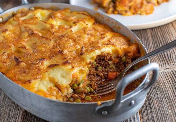 Shepherds Pie in a rustic casserole dish Traditional fresh and homemade cooked Shepherds pie. Served in a old fashioned roasting pan on wooden table background comfort food stock pictures, royalty-free photos & images