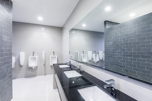 Contemporary public Interior of bathroom with sink basin faucet lined up with big mirror and public toilet urinals Modern design.