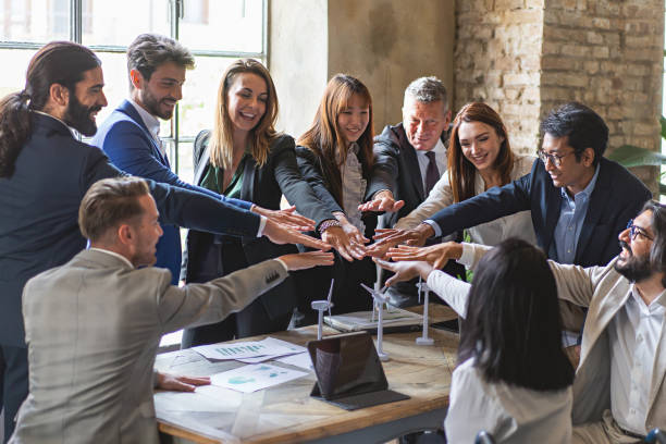 empresários multiétnicos unindo as mãos em pé ao redor da mesa do escritório - trabalho em equipe alto cinco o sucesso de um projeto sustentável de economia verde - high culture - fotografias e filmes do acervo