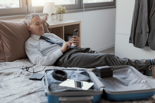 Businessman traveling for work, he is using his smartphone in the hotel room and searching online services