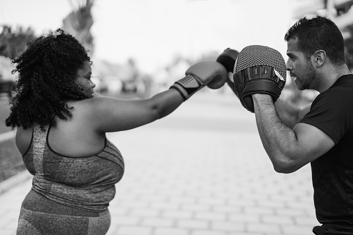African curvy woman and personal trainer doing boxing workout session outdoor