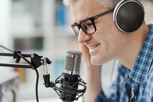 Smiling man wearing headphones and recording audio podcast using a professional microphone