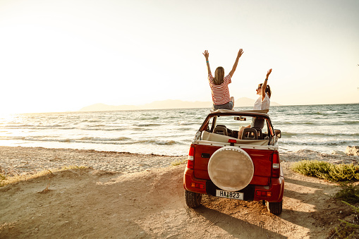 Two cheerful young women enjoying a summer’s road trip. The are looking at the view and enjoying