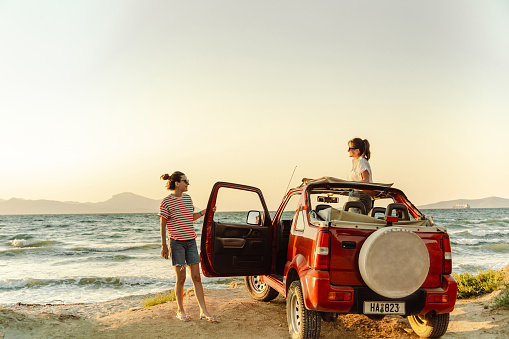 Two cheerful young women enjoying a summer’s road trip. They are looking at the view and enjoying