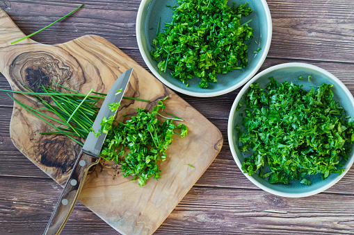 Fresh and chopped spicy parsley and chives herbs on cutting board, top view, copy space