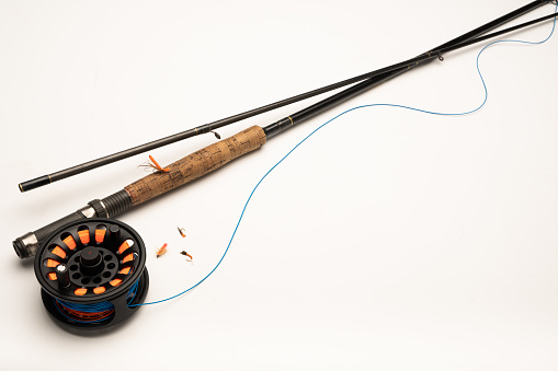 Fly fishing reel, rod, and flies on a white background with copy space
