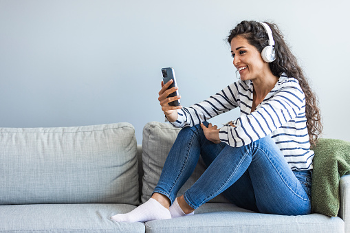 Having fun listening to music. Beautiful woman enjoying in her bed and listening to the music. Side view of content woman listening to music on headphones at home