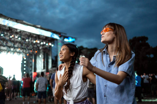 Music festival Two Asian and Caucasian girls dance in front of a stage and enjoy the atmosphere at a music festival. concert stock pictures, royalty-free photos & images