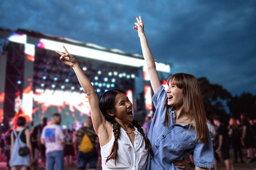 Two Asian and Caucasian girls dance in front of a stage and enjoy the atmosphere at a music festival.