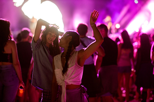 Two Asian and Caucasian girls dance in the crowd and enjoy the atmosphere at a music festival.