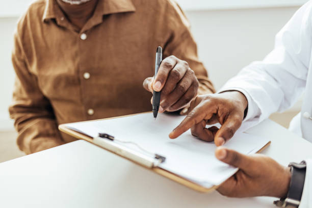 homme ayant une visite au bureau du médecin masculin - remplir un formulaire photos et images de collection