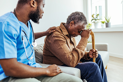 Male professional doctor touching shoulder, comforting upset senior patient, having geriatric disease, expressing trust and support.