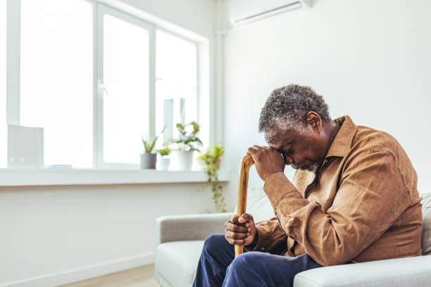 uomo anziano premuroso seduto da solo a casa con il suo bastone da passeggio - men senior adult serious depression foto e immagini stock