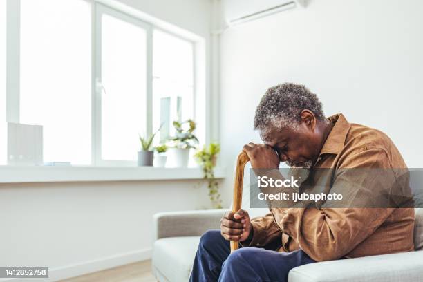 Thoughtful Elderly Man Sitting Alone At Home With His Walking Cane Stock Photo - Download Image Now