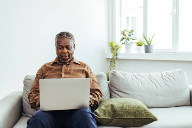 istock Smiling Senior Man Sitting On Sofa Using Laptop At Home 1412852824