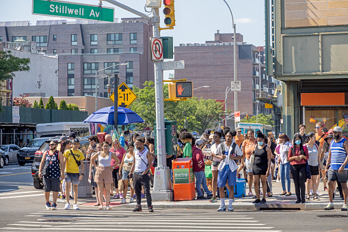 Coney Island, Brooklyn, NY, USA - June 25, 2022: Large crowd of pedestrians waiting for the traffic light to change to cross the Surf Avenue on a hot summer afternoon